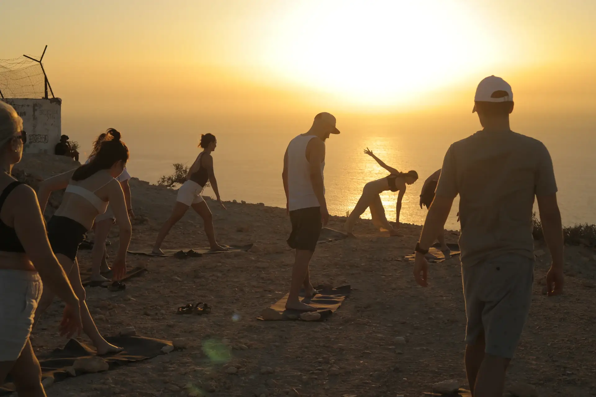 People practising yoga on a cliff at sunset, the ocean behind them